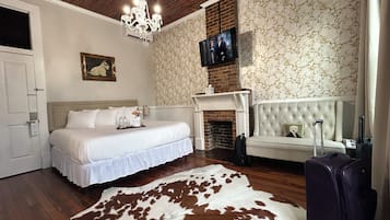 A hotel room with a bed, a fireplace, a television, a sofa, and a suitcase.