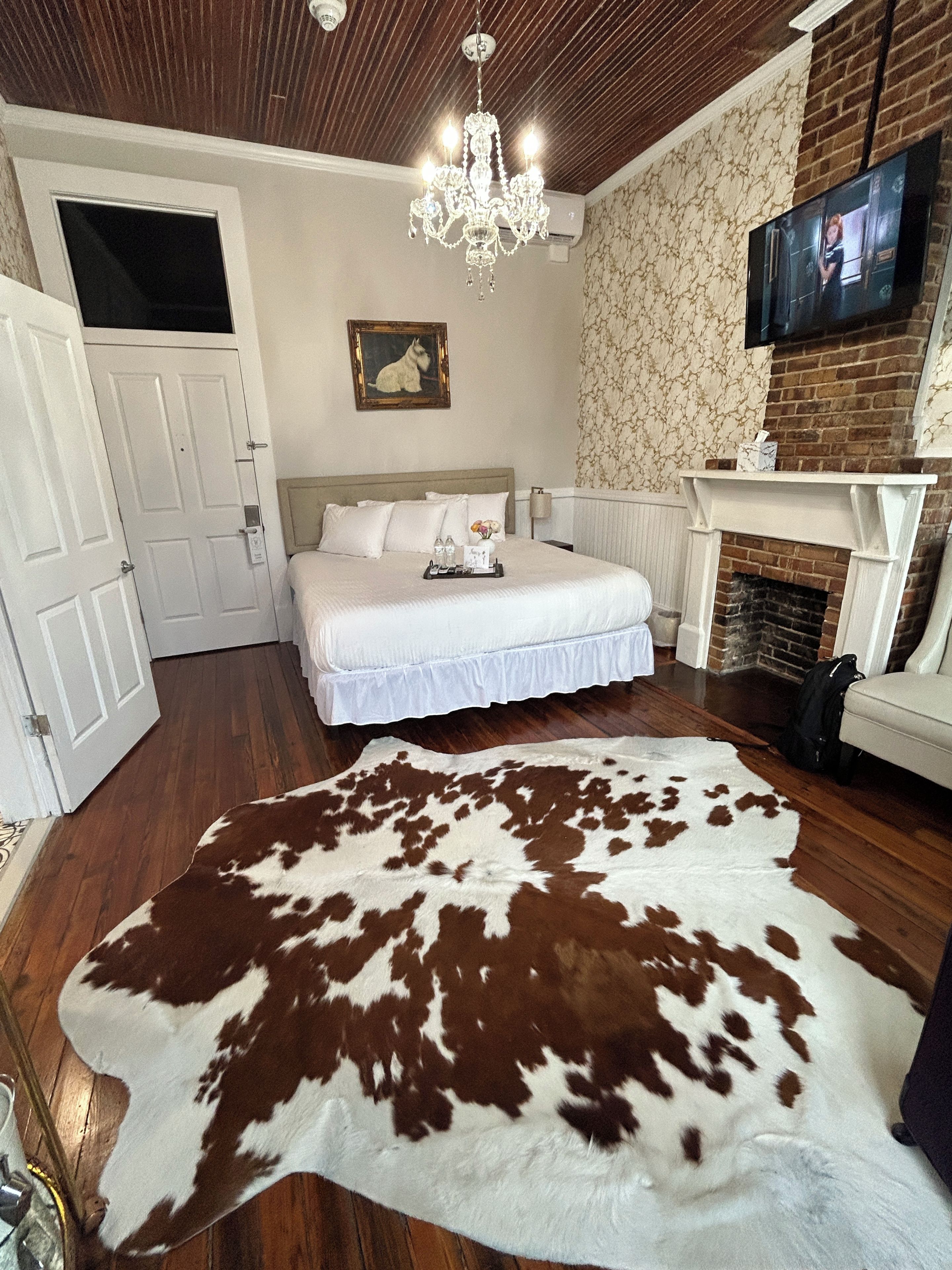 Un dormitorio con una cama grande, una araña, una chimenea y una alfombra de cuero de vaca.