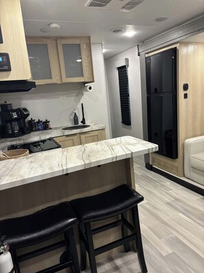Cozinha moderna com bancada de mármore, banquetas pretas e geladeira preta.