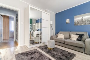 Ett modernt vardagsrum med en grå soffa, en stor spegel och en tavla som föreställer en stadsbild på väggen.
