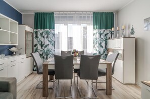 A dining area with a table, chairs, and a view through sheer curtains. - Bogedaina Central Apartment (Chorzów)
