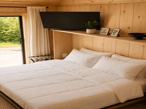 A bed with white bedding in a room with wooden walls and a television on a shelf. - Modern Creekside Cabin w/ Hot Tub — Near Smoky's (Cosby)