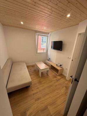 Een knus ingerichte kamer met houten plafond, een bank, een eettafeltje en een televisie aan de wand.