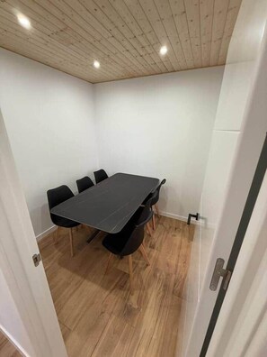 Een kamer met een houten plafond, een zwarte tafel met stoelen en een witte deur.