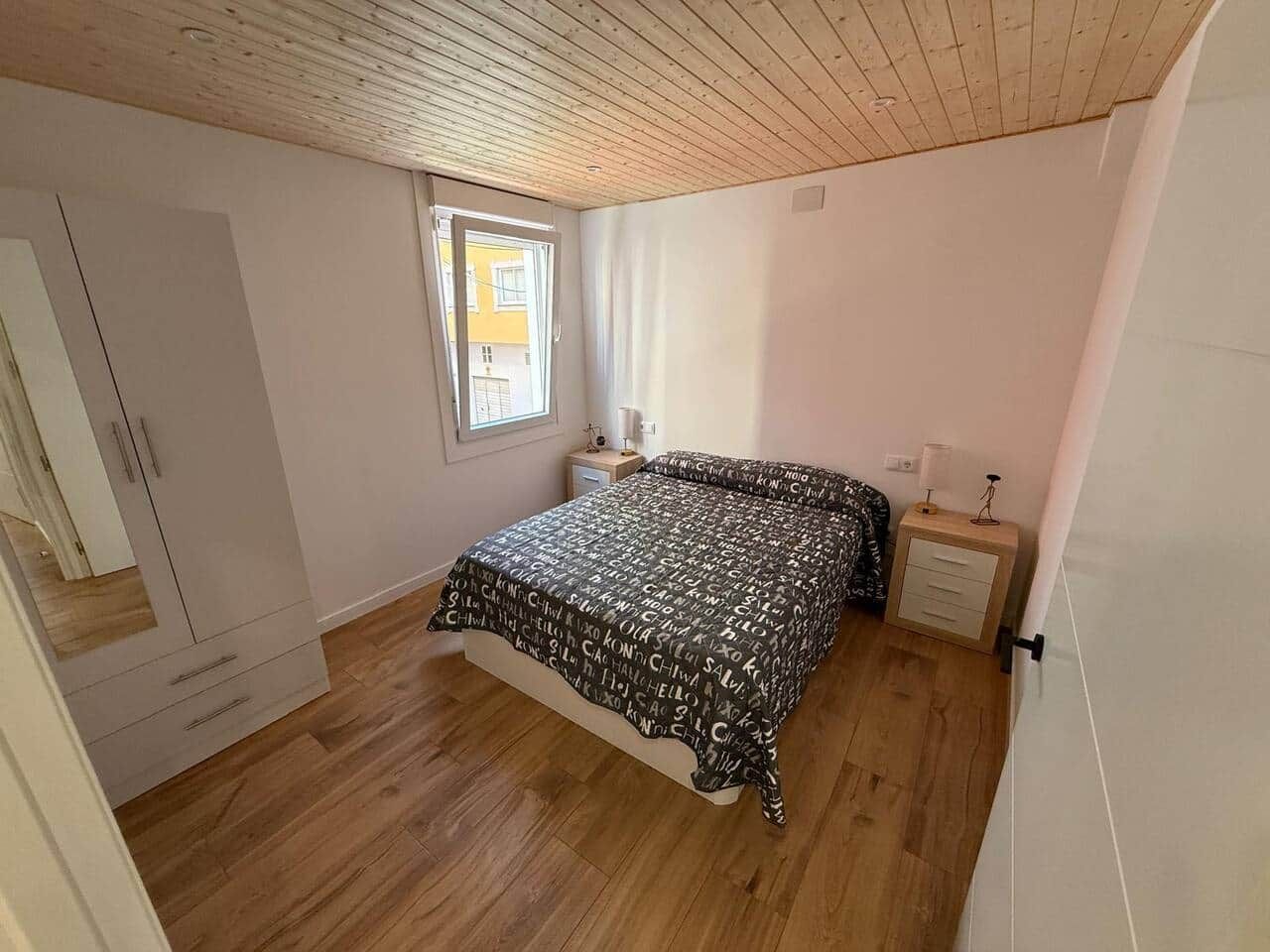 Un dormitorio con cama, armario, mesita de noche y ventana.
