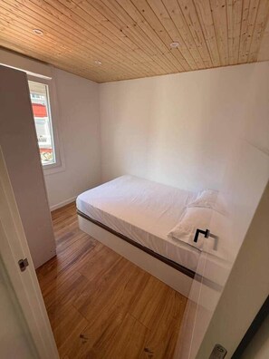 Een kleine kamer met een enkel bed, houten vloer en een schuine balkenkap.