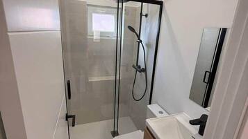 Un baño pequeño con ducha de vidrio, inodoro blanco y tocador de madera con espejo.