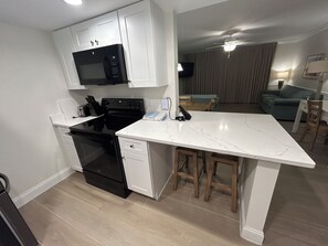 A modern kitchen with a built-in microwave, stove, and dishwasher, a marble countertop, and wooden stools. - Newly Renovated Beach Escape with Pool on Fort Myers Beach (Fort Myers Beach)