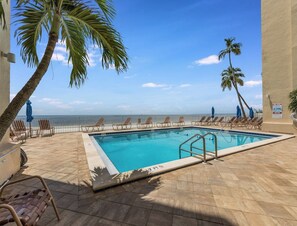 A pool area with a clear view of the ocean, palm trees, and lounge chairs. - Newly Renovated Beach Escape with Pool on Fort Myers Beach (Fort Myers Beach)