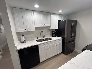 A kitchen with white cabinets, a black dishwasher, a stainless steel sink, and a black refrigerator. - Newly Renovated Beach Escape with Pool on Fort Myers Beach (Fort Myers Beach)