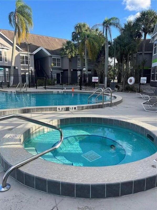 A swimming pool with a circular design, surrounded by a tiled deck and palm trees. - Ground-floor Disney condo with resort pool (Kissimmee)