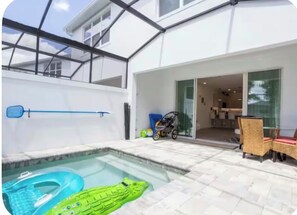 A swimming pool with inflatable toys, a covered patio area, and a glimpse of the interior through glass doors. - Cozy house /Pool heater/3 beds (Clermont)