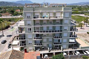 A multi-story residential building with balconies, a rooftop terrace, and a parking area. - Apartment with pool, 300 m from Piles beach (Piles)
