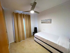 A room with a bed, a ceiling fan, a chair, and a wall-mounted picture. - Apartment with pool, 300 m from Piles beach (Piles)