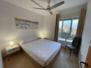 Ein Hotelzimmer mit einem Bett, einem Sessel, einem Deckenventilator, einem Gemälde und einem Fenster mit Blick.