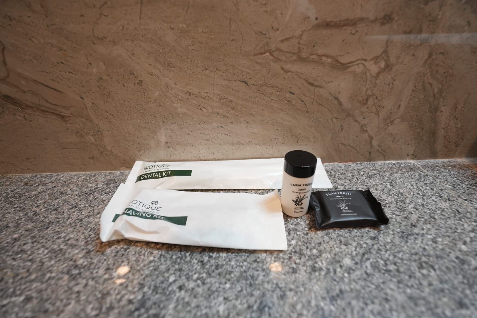 Une trousse de soins dentaires, une trousse de rasage et une pochette noire sur un comptoir en granit.