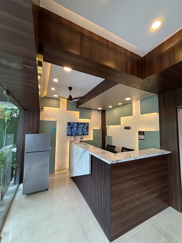 A modern hotel reception area with a marble counter, a refrigerator, and a ceiling fan.