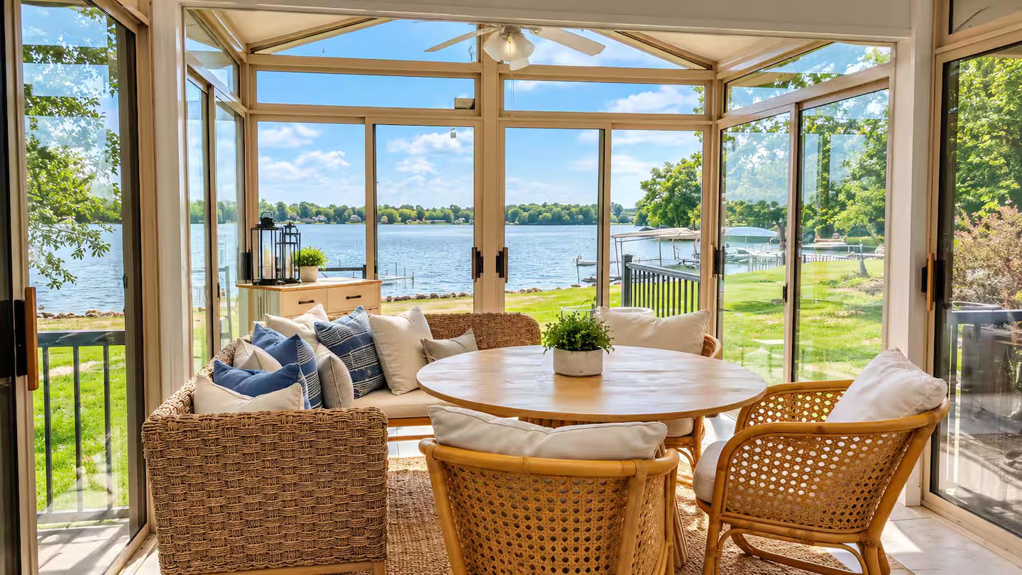 Un invernadero con vistas a un lago, muebles de mimbre y una mesa con una planta.
