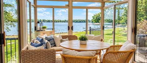Un invernadero con vistas a un lago, muebles de mimbre y una mesa con una planta.