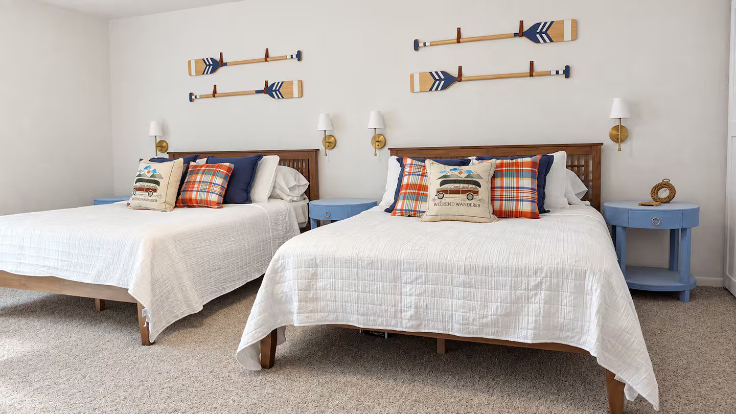A hotel room with two beds, each with a white bedspread, and matching nightstands with lamps.