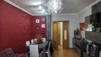 Un comedor con pared roja, una araña y una cocina moderna con electrodomésticos integrados.