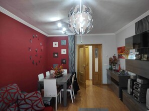 A dining area with a red wall, a chandelier, and a modern kitchen with built-in appliances.