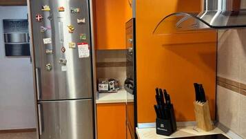 Cocina compacta con refrigerador de acero inoxidable, horno empotrado y bloque de cuchillos.