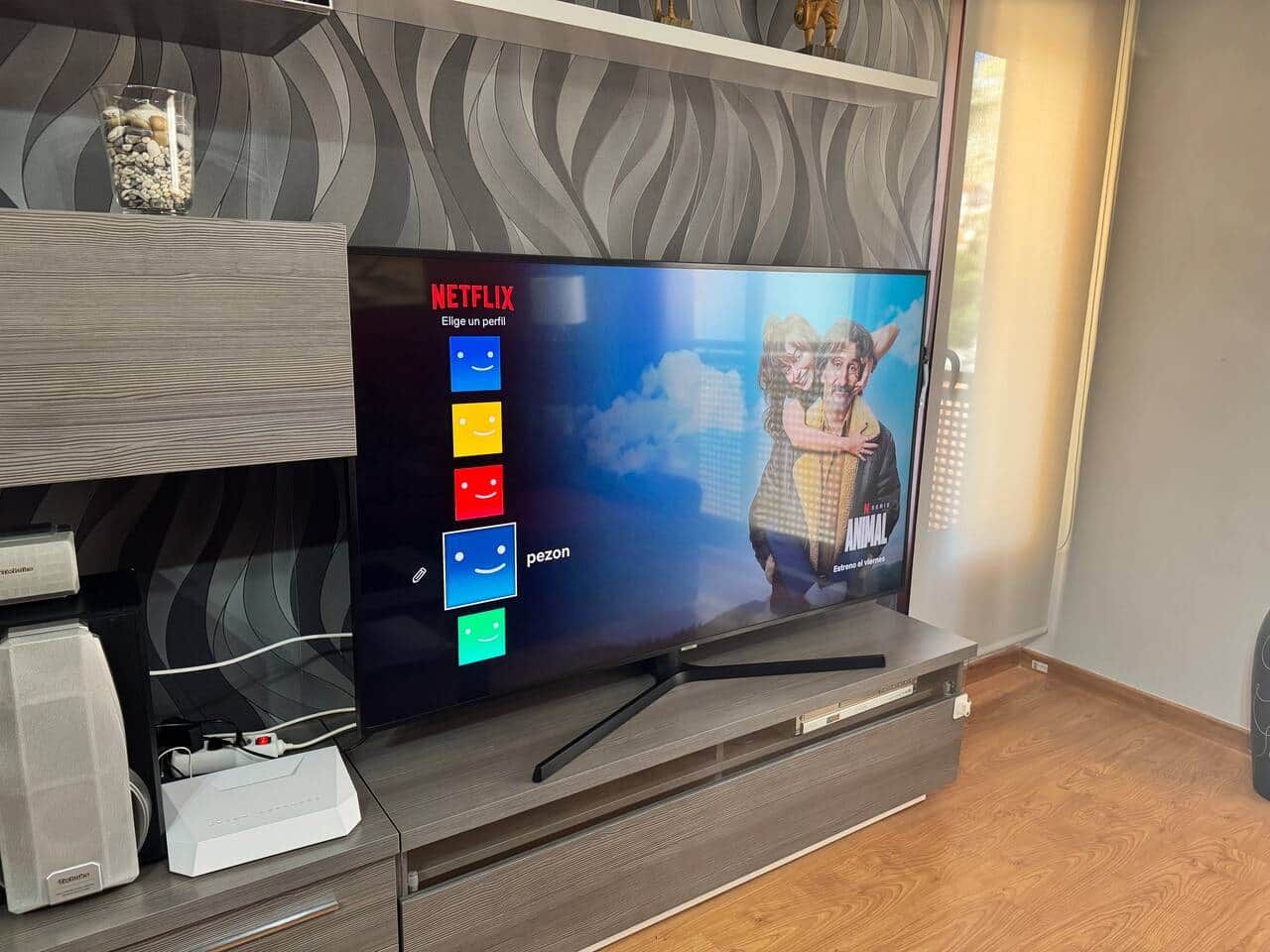 Una sala de estar moderna con un televisor de pantalla plana mostrando la interfaz de Netflix, una mesa de centro de vidrio con objetos decorativos y un mueble de entretenimiento de madera.