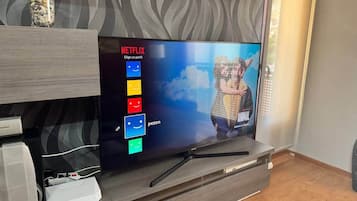 Una sala de estar moderna con un televisor de pantalla plana mostrando la interfaz de Netflix, una mesa de centro de vidrio con objetos decorativos y un mueble de entretenimiento de madera.