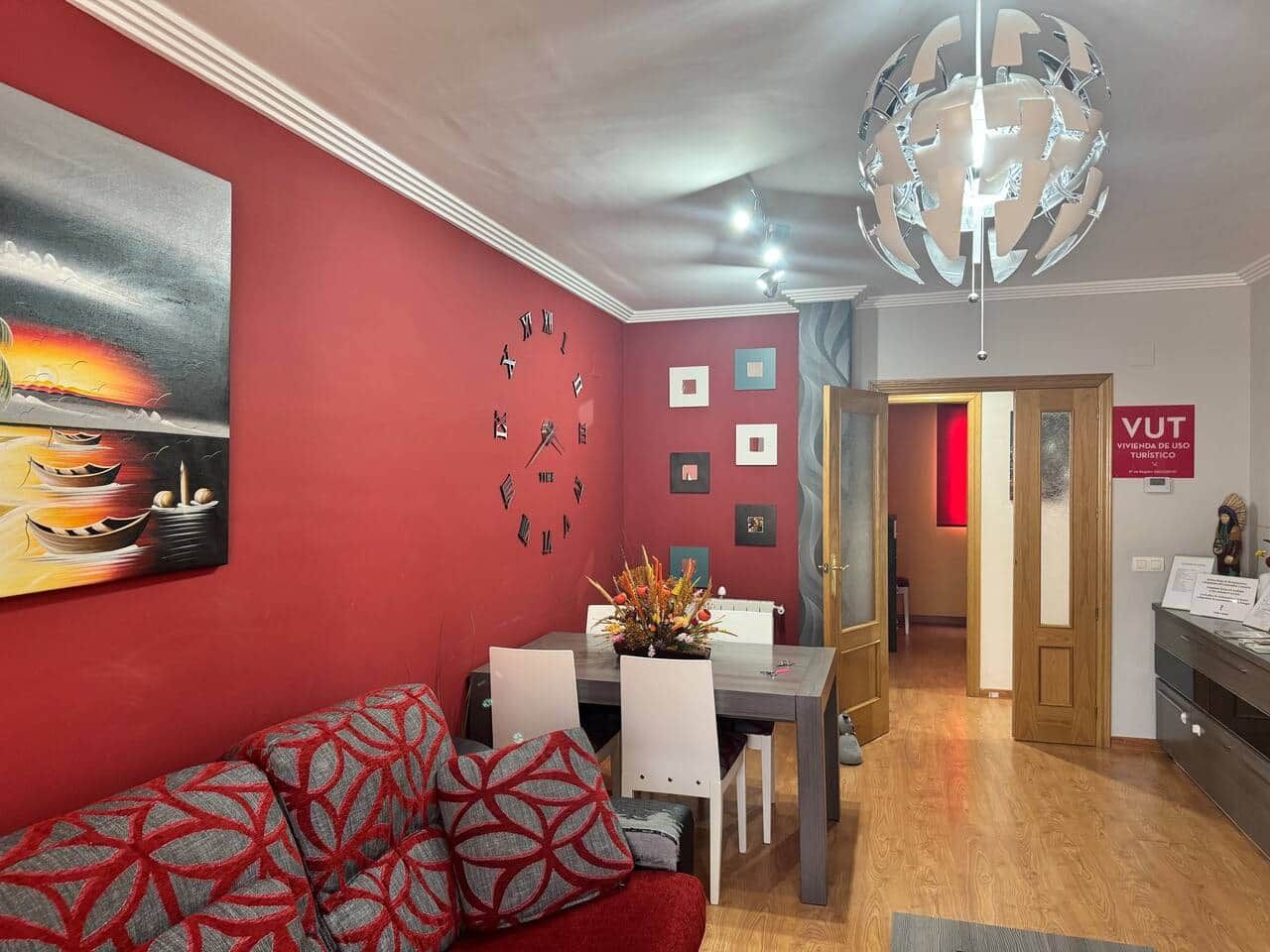 A modern living room with a red wall, a dining area, and a hallway leading to a door labeled "VUT".