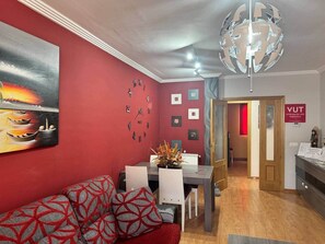 A modern living room with a red wall, a dining area, and a hallway leading to a door labeled "VUT".