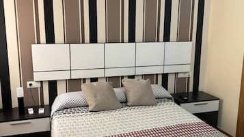 Habitación de hotel ordenada con una cama grande, una mesita de noche con lámpara y una pared con rayas verticales.