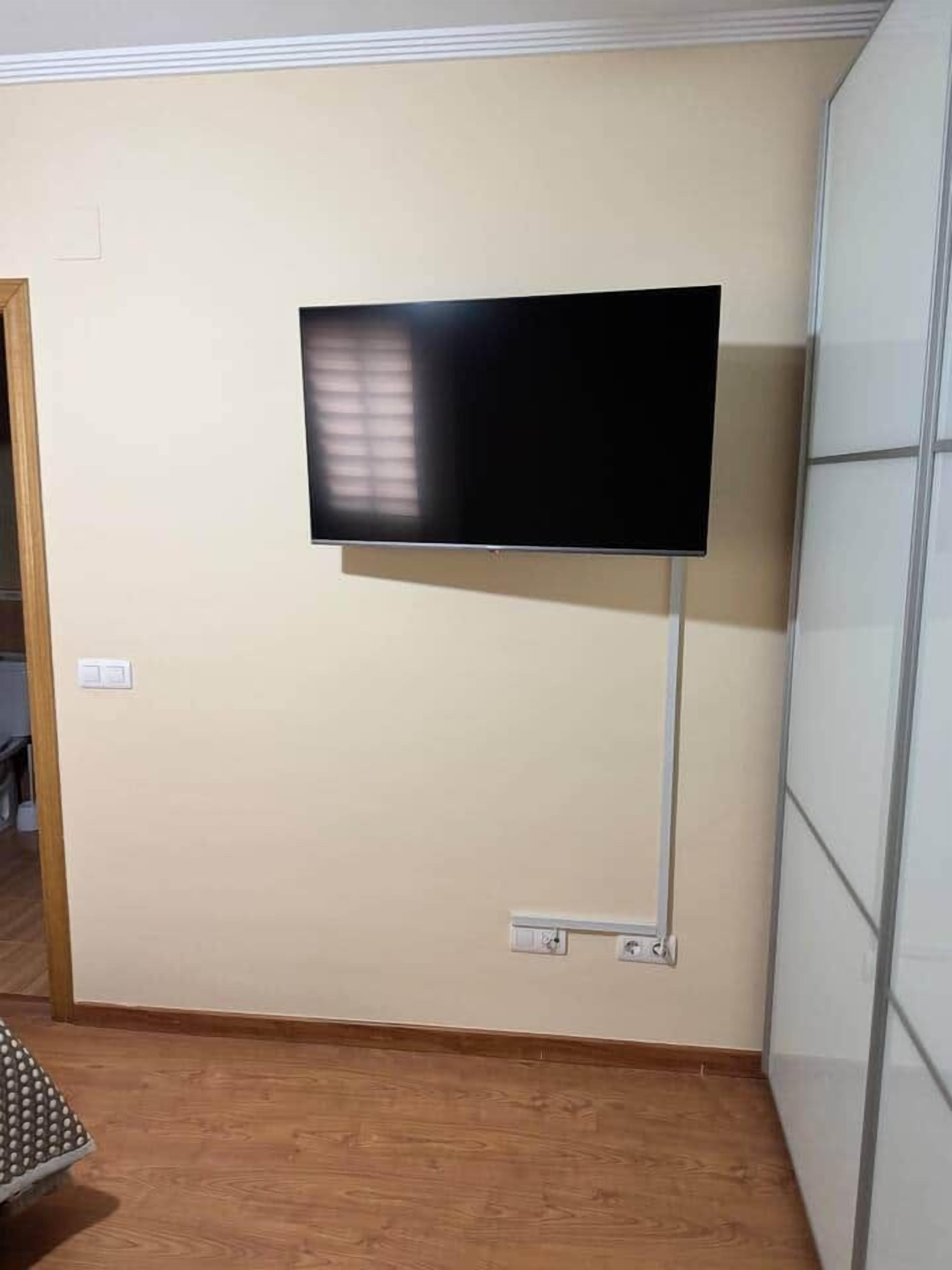 Une pièce avec un téléviseur à écran plat fixé au mur, un plancher en bois et une armoire blanche.
