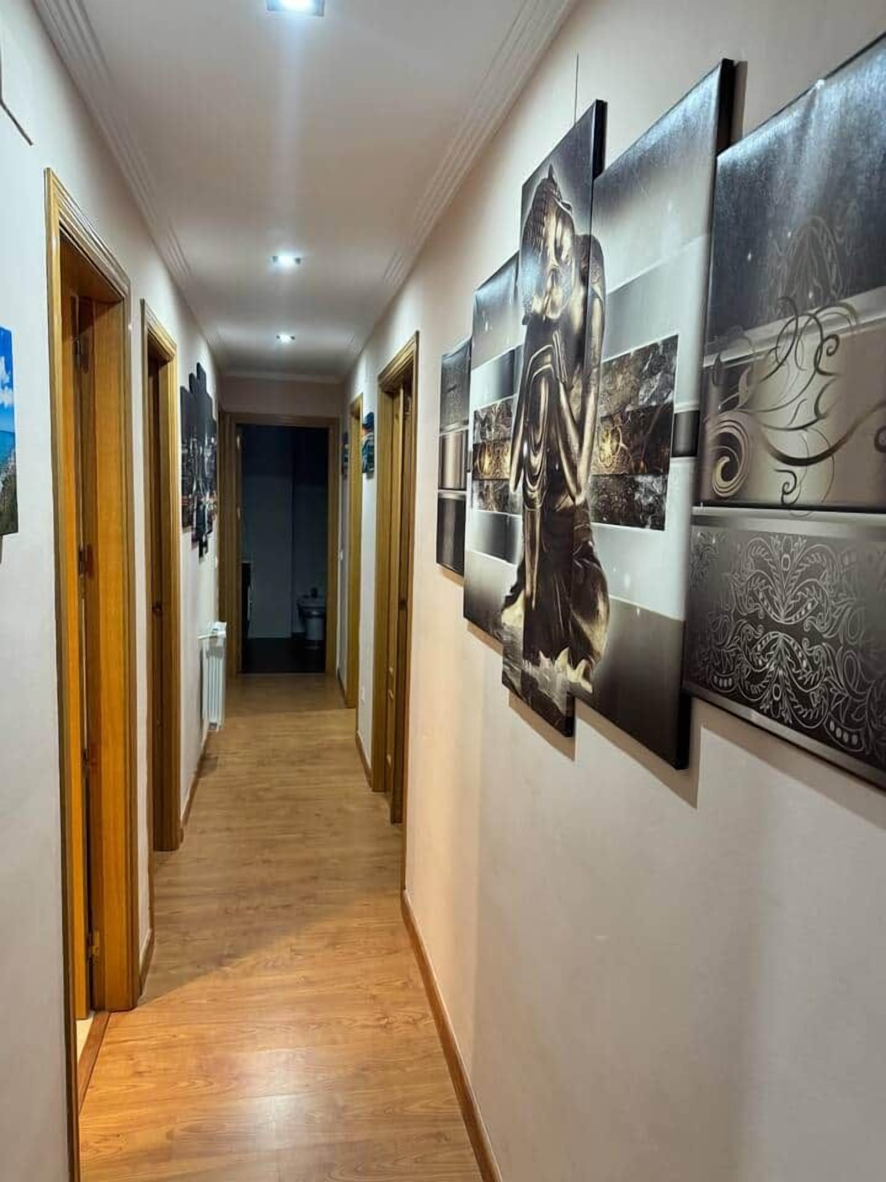 Un pasillo con suelo de madera y paredes decoradas con obras enmarcadas.