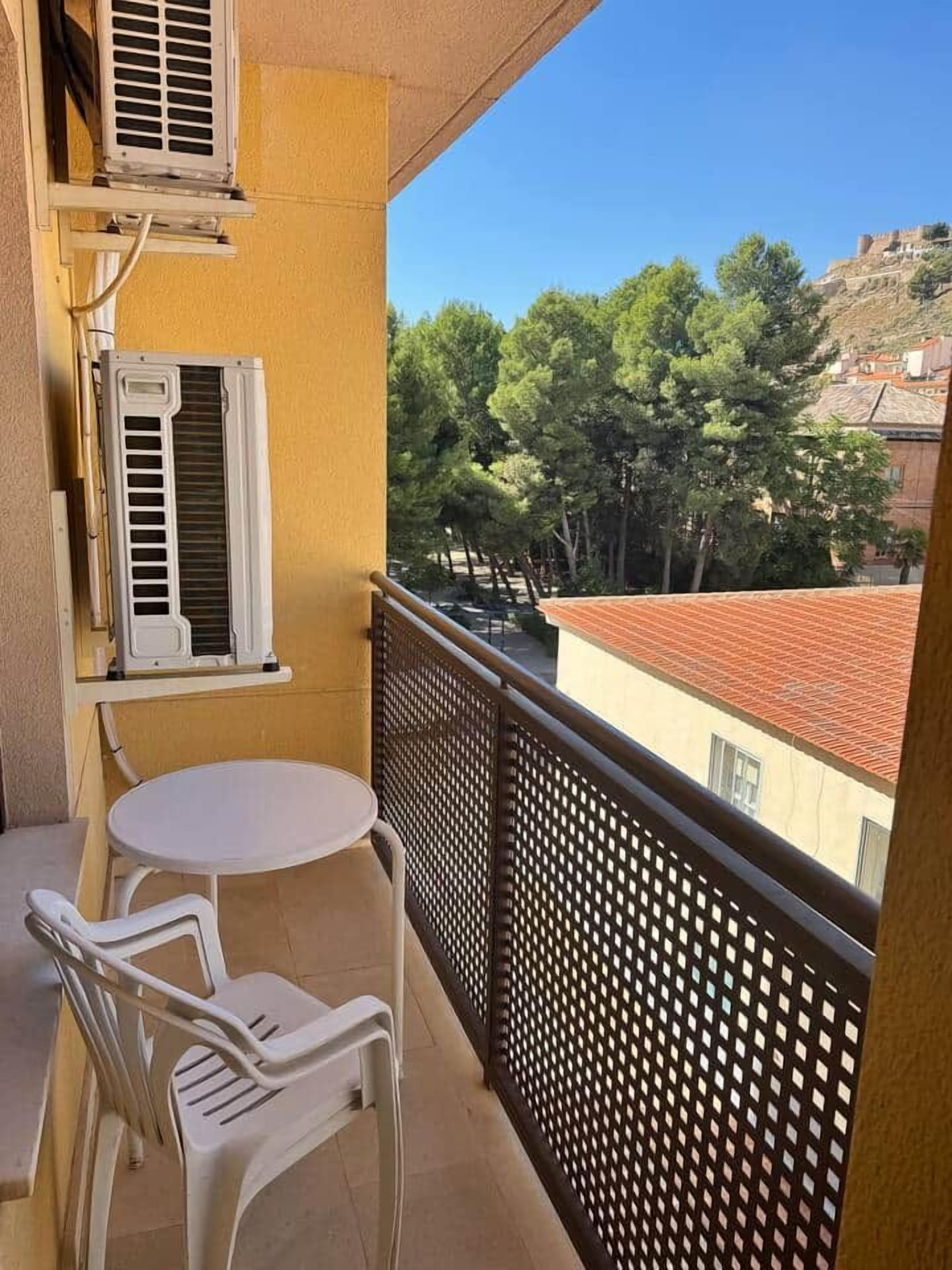 Un balcón con mesa y sillas, con vistas a una zona residencial con árboles y edificios.