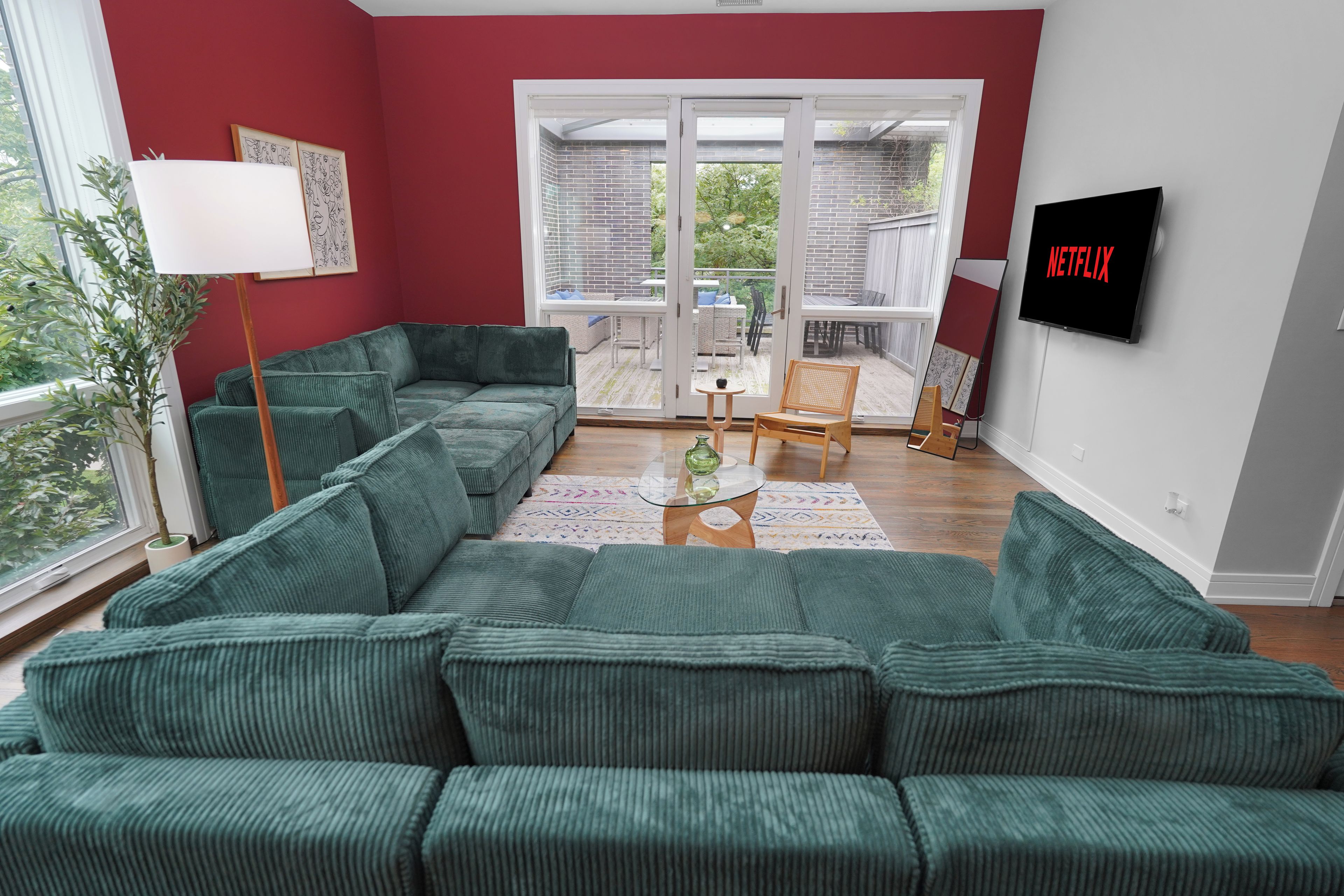 A living room with a green sofa, a TV, and a balcony with a view.