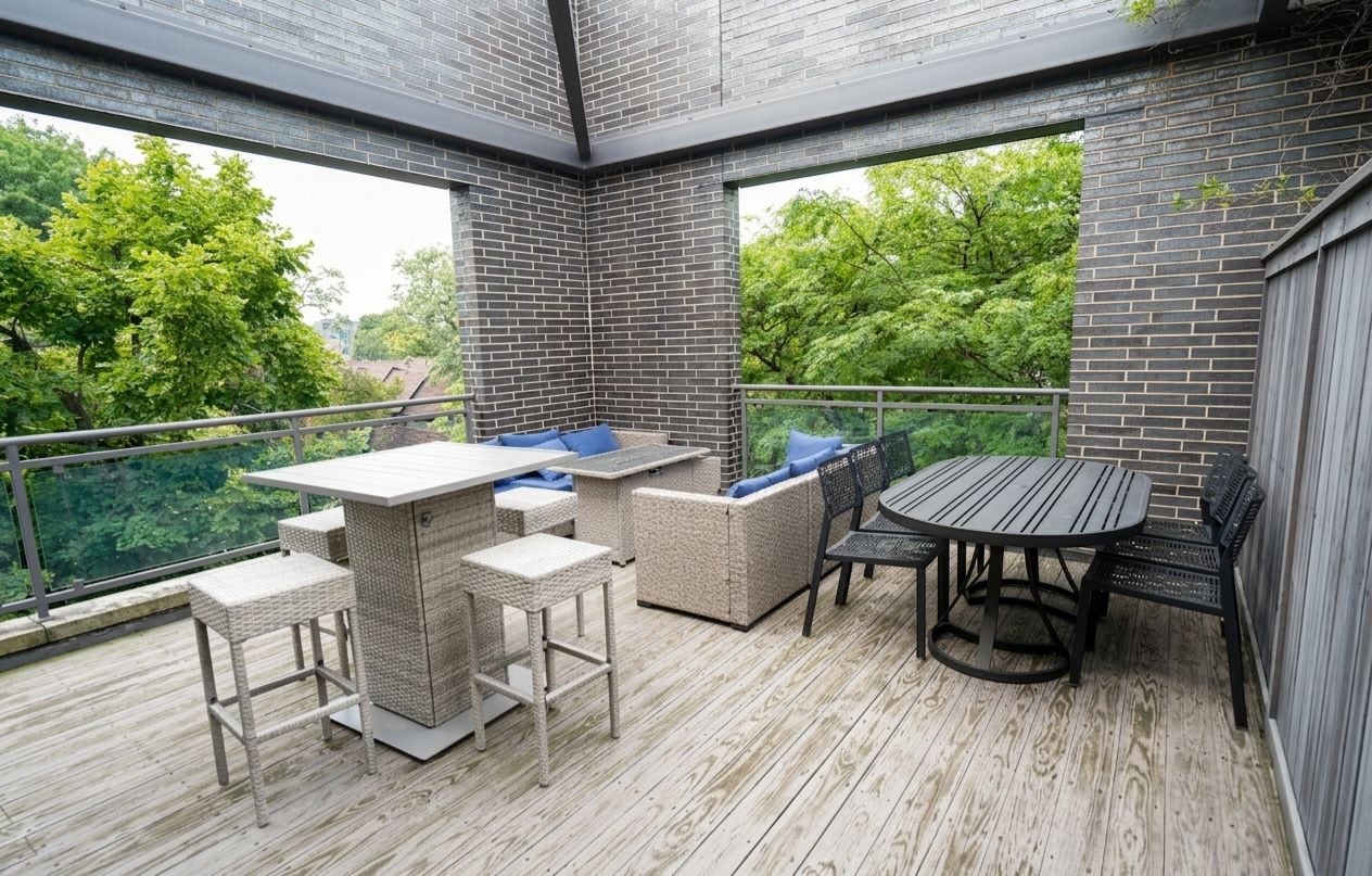 An outdoor deck with a table and chairs, surrounded by brick walls and overlooking a green landscape.