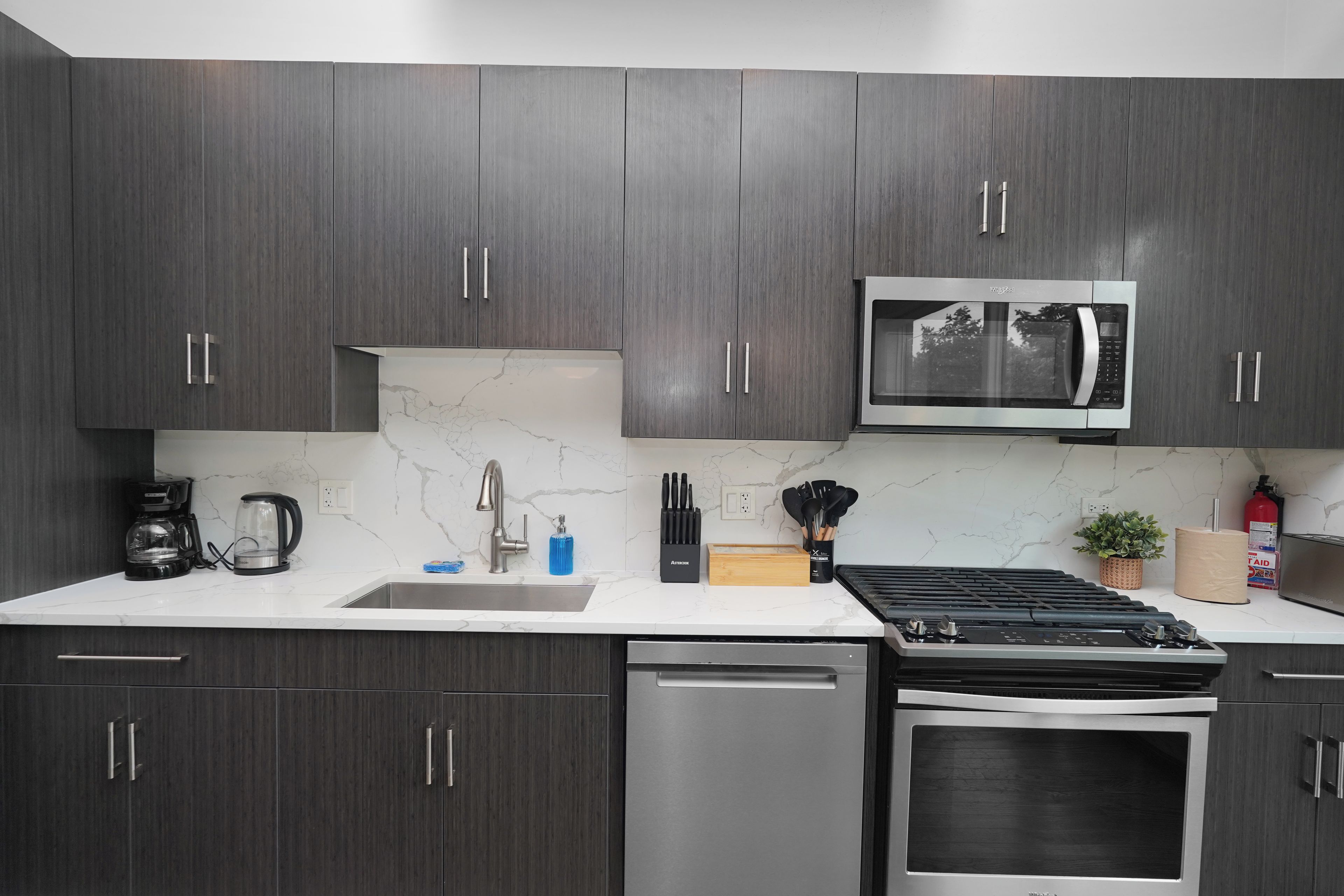 A modern kitchen with dark wood cabinets, a stainless steel microwave, a coffee maker, and a dishwasher.