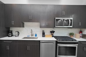A modern kitchen with dark wood cabinets, a stainless steel microwave, a coffee maker, and a dishwasher. - Little Italy 4BR Retreat w/ Optional Parking (Chicago)