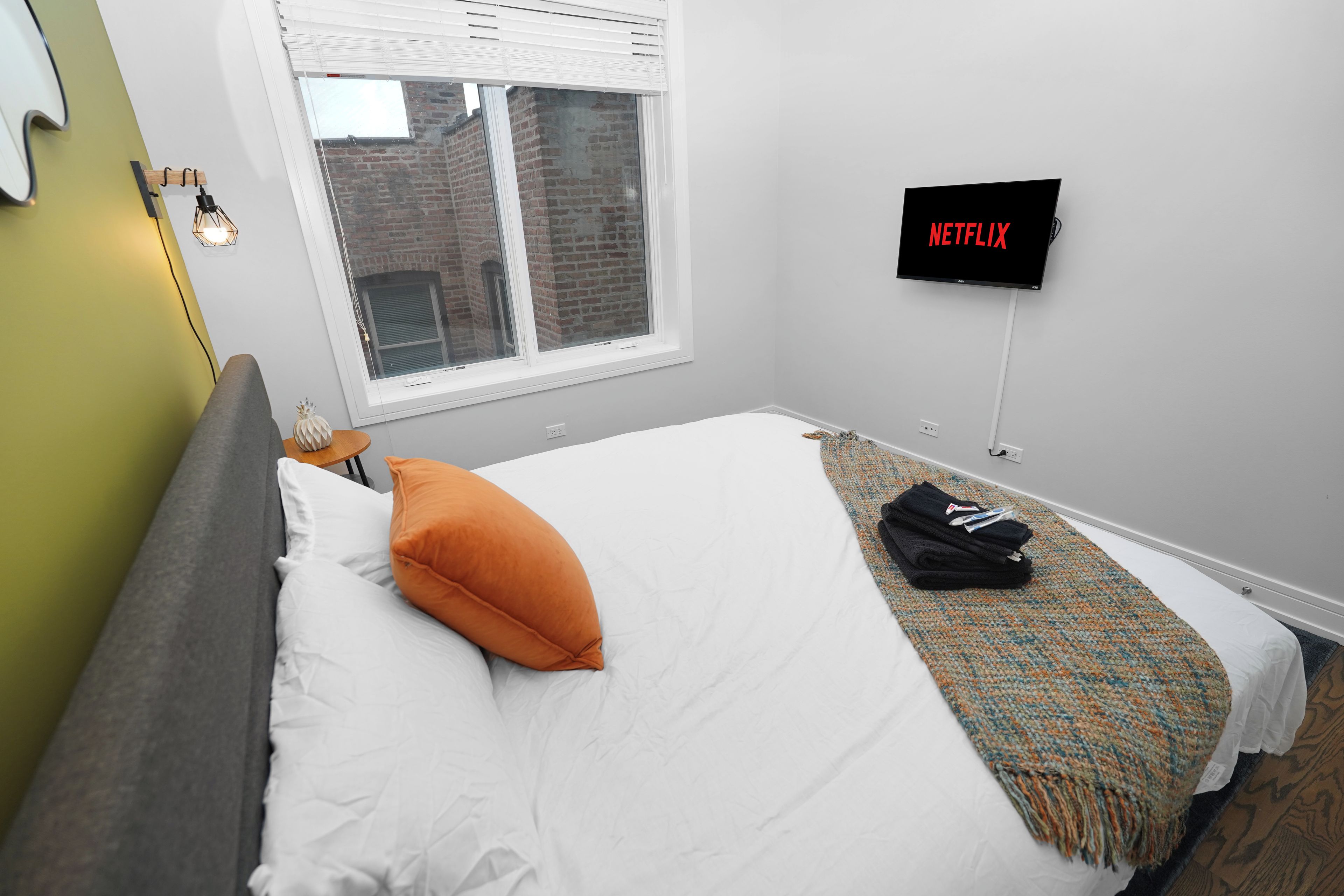 A hotel room with a bed, a window, a wall-mounted TV, and a bedside table.