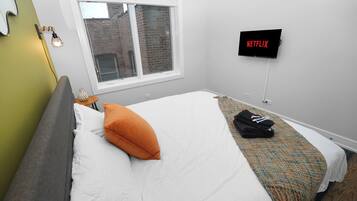 A hotel room with a bed, a window, a wall-mounted TV, and a bedside table.