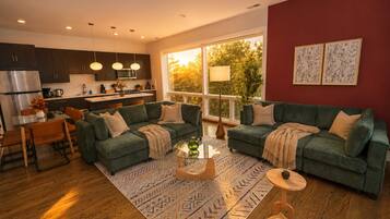 A modern living room with a green sofa set, a glass coffee table, and a dining area with a wooden table and chairs.