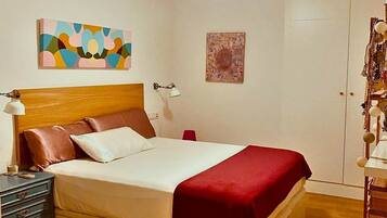 A bedroom with a bed, a nightstand, a lamp, a ceiling fan, and artwork on the walls.