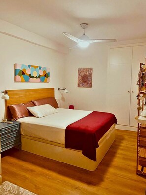 A bedroom with a bed, a nightstand, a lamp, a ceiling fan, and artwork on the walls. - Renovated 3-bedroom apartment · Conde de Ureña, Málaga (Málaga)