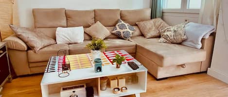 Una sala de estar moderna con un sofá color beige, una mesa de centro blanca con un patrón geométrico colorido y dos cuadros abstractos en la pared.