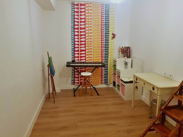 A room with a wooden floor, a white desk, a stool, a keyboard, a painting on an easel, and a colorful curtain. - Renovated 3-bedroom apartment · Conde de Ureña, Málaga (Málaga)