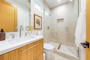 Een moderne badkamer met een houten wastafelmeubel, een grote spiegel, een toilet en een douchecabine met glazen wanden.