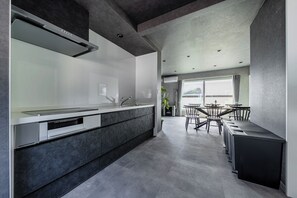 Una cocina moderna con una isla central, una zona de comedor con mesa y sillas, y vistas a través de una ventana.