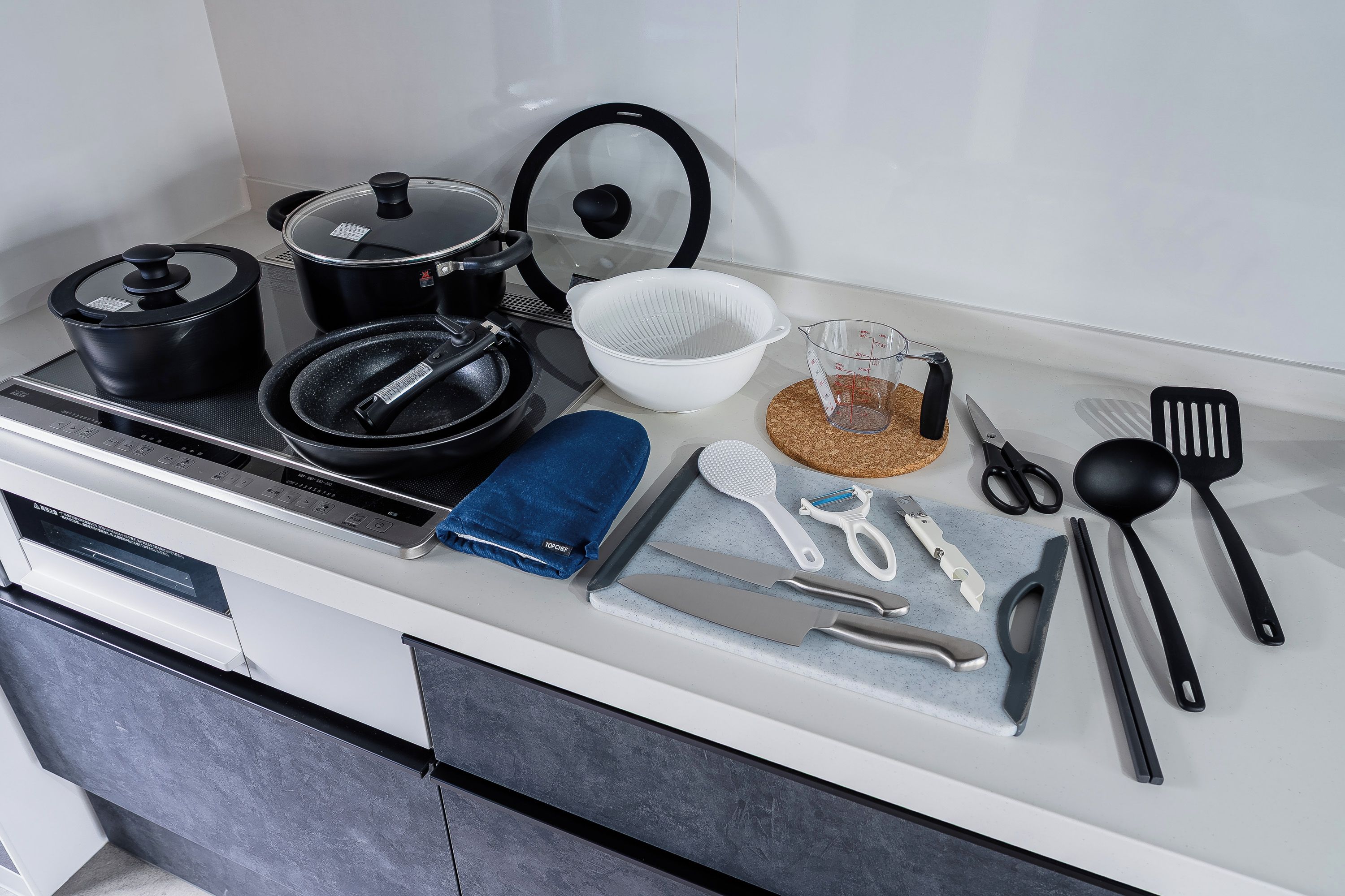A kitchen counter with various cooking utensils, a pot, a colander, and a measuring cup.