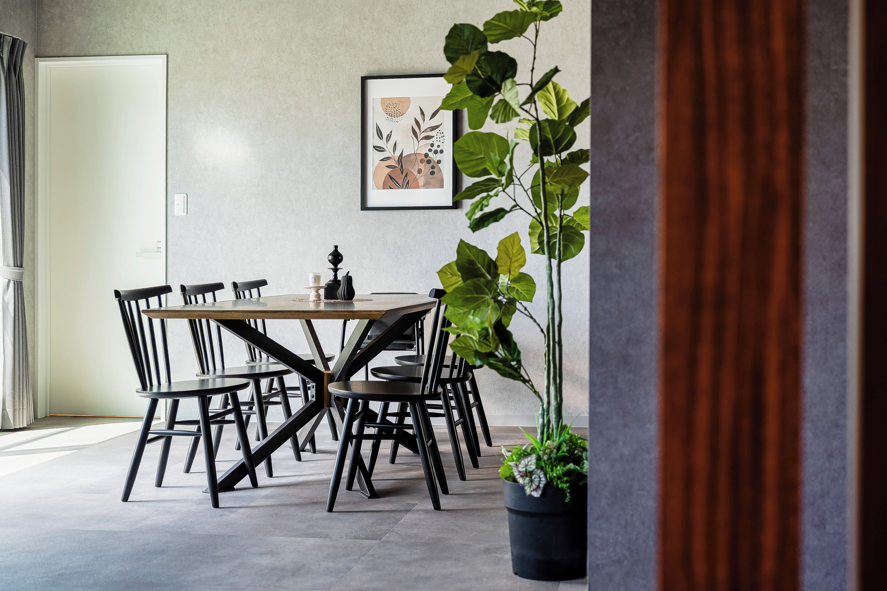 A dining area with a round table and chairs, a potted plant, and a framed artwork on the wall.